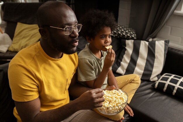 Padre comiendo palomitas de maíz con su hijo en el sofá de casa