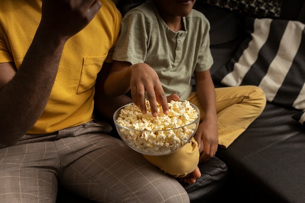 Padre comiendo palomitas de maíz con su hijo en el sofá de casa