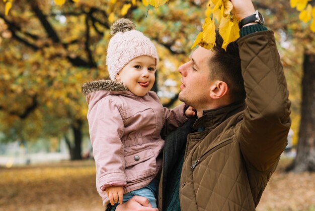 Padre demostrando su hija follaje de otoño en el bosque