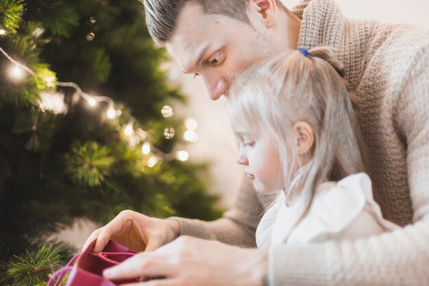 Padre e hija al lado de árbol de navidad iluminado