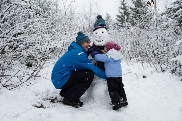 Padre e hija alegre haciendo muñeco de nieve