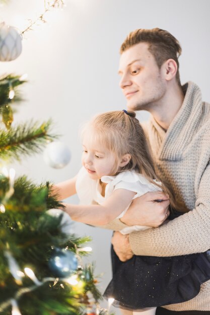 Padre e hija decorando árbol de navidad iluminado juntos