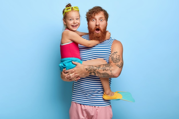 Padre e hija de jengibre estupefactos posando en trajes de piscina