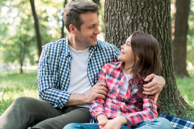 Padre e hija mirándose sentados cerca de un árbol