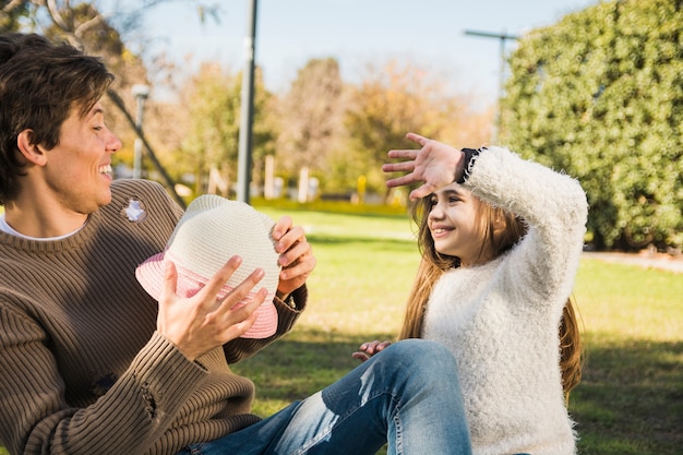 Padre e hija sentados en el parque jugando con sombrero