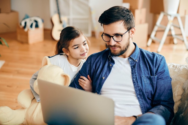 Padre e hija sonrientes usando una laptop en su nuevo hogar