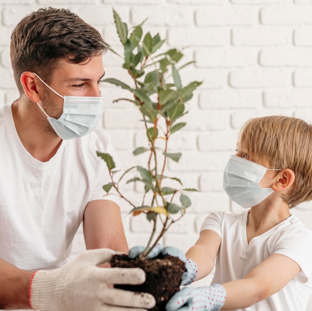 Padre e hijo aprenden a plantar juntos en casa mientras usan máscaras médicas