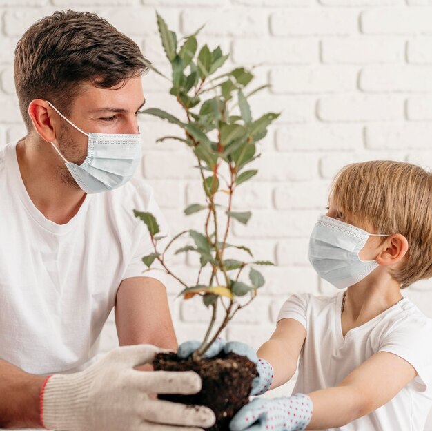 Padre e hijo aprenden a plantar juntos en casa mientras usan máscaras médicas