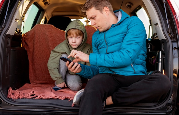 Padre e hijo en el coche con smartphone durante un viaje por carretera