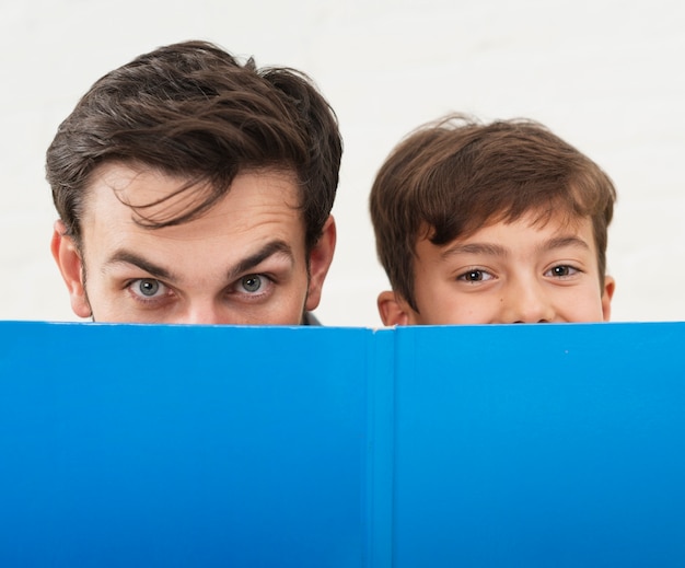 Padre e hijo cubriéndose la cara con un libro azul