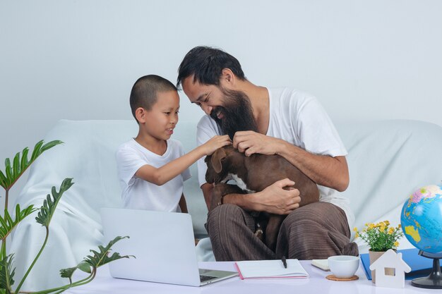 Padre e hijo juegan a un perro mientras trabajan en el sofá de casa.