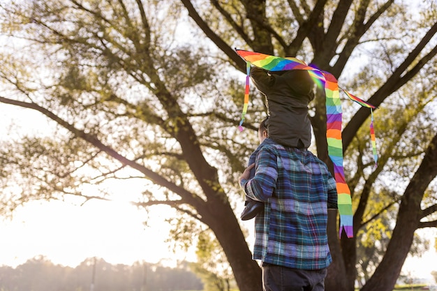 Padre e hijo jugando con una cometa desde atrás shot