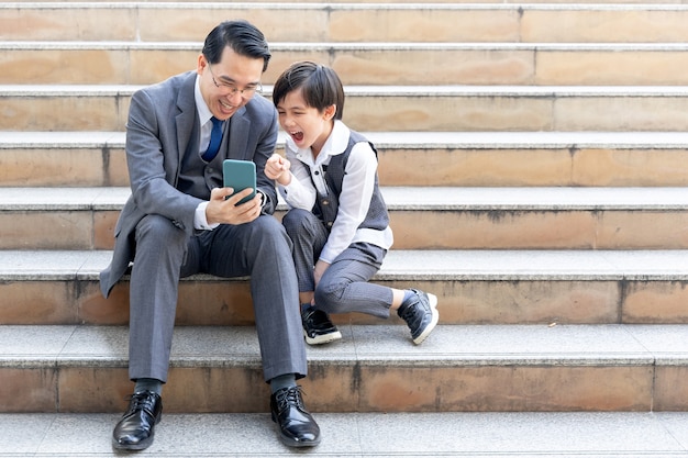 Foto gratuita padre e hijo jugando con teléfonos inteligentes juntos en el distrito de negocios urbano