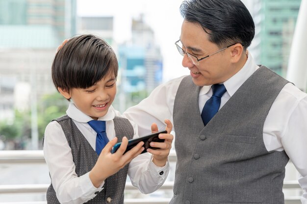 Padre e hijo jugando con teléfonos inteligentes juntos en el distrito de negocios urbano