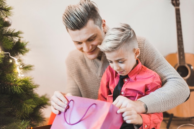 Padre e hijo mirando en bolsa al lado de árbol de navidad