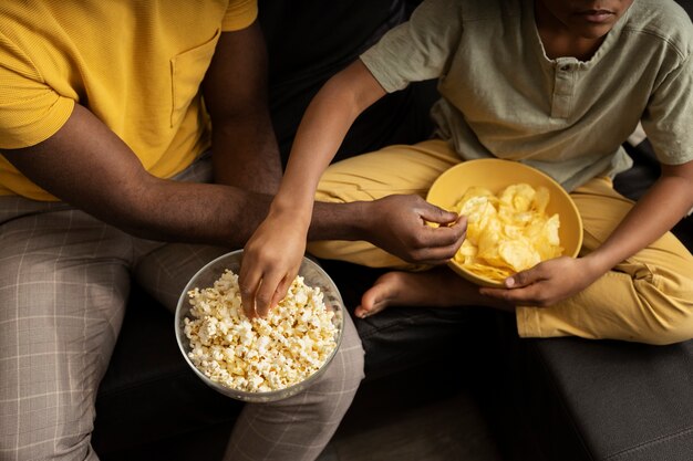 Padre e hijo con palomitas de maíz y papas fritas juntos en el sofá