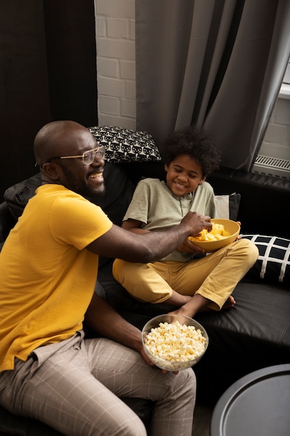 Foto gratuita padre e hijo con palomitas de maíz y papas fritas juntos en el sofá