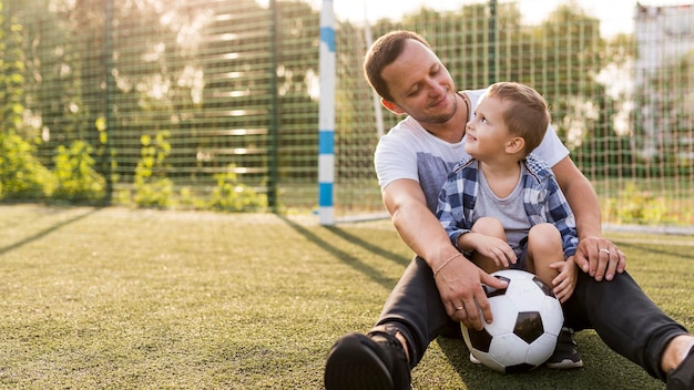 Foto gratuita padre e hijo sentados en el campo de fútbol