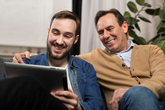 Padre e hijo sonriendo y mirando la tableta en la sala de estar