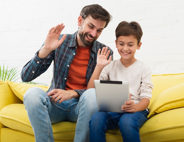 Padre e hijo sosteniendo una tableta y saludando