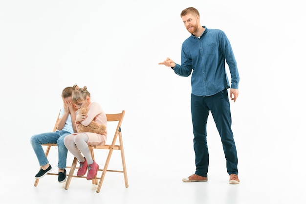 Padre enojado regañando a su hijo e hija en casa. Foto de estudio de familia emocional. Las emociones humanas, la infancia, los problemas, los conflictos, la vida doméstica, el concepto de relación