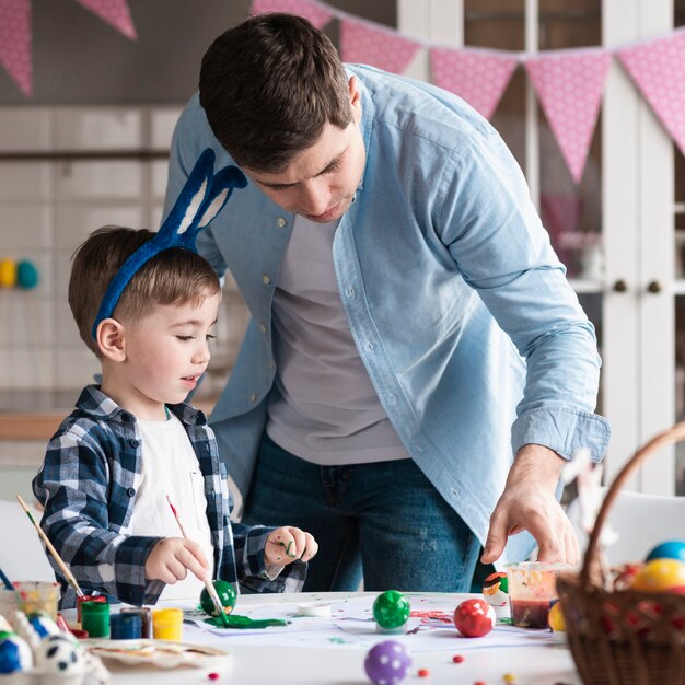 Padre enseñando a niño a pintar huevos de pascua