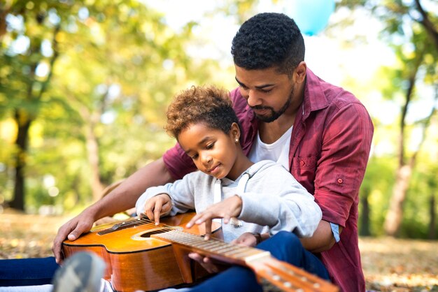 Padre enseñando a su adorable hija a tocar la guitarra en el parque