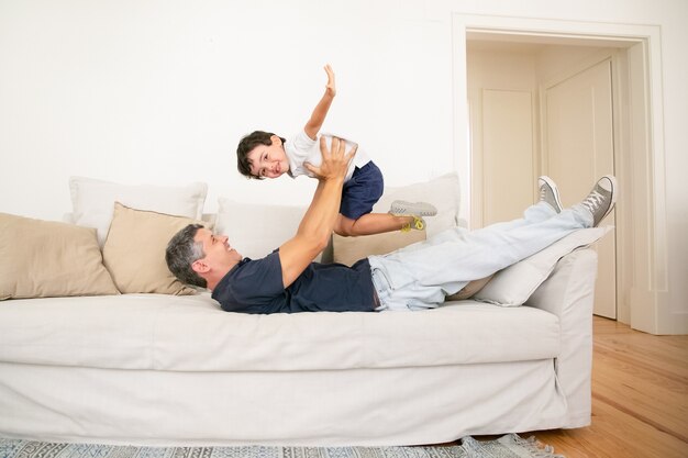 Padre feliz acostado en el sofá y jugando con su hijo.