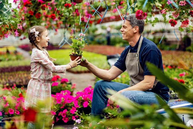 Padre feliz dándole a su pequeña hija una flor en maceta mientras ella lo ayuda en un centro de jardinería