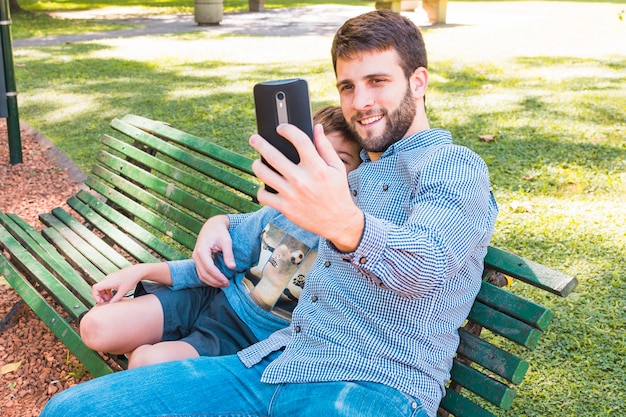Padre feliz que toma el selfie con su hijo en el teléfono móvil en el parque