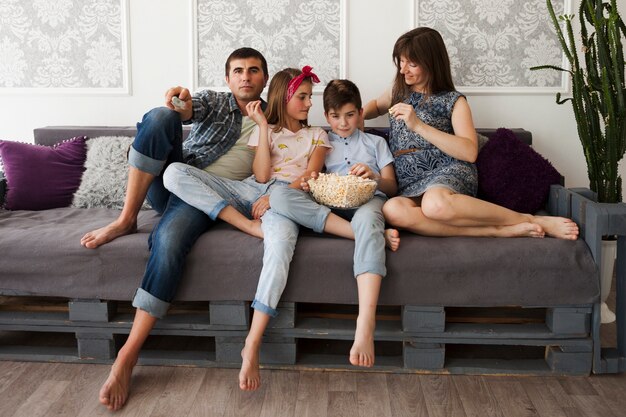 Padre feliz con sus hijos sentados en el sofá y comiendo palomitas de maíz