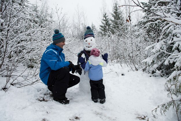 Padre feliz viendo hija haciendo muñeco de nieve