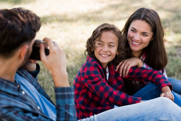 Padre fotografiando a madre e hijo al aire libre en el parque