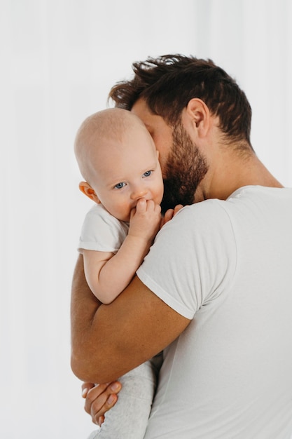 Foto gratuita padre guapo sosteniendo y besando a su bebé