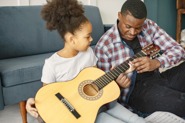 Padre con hija en el sofá. Chica sosteniendo una guitarra. Aprendiendo a tocar la guitarra.