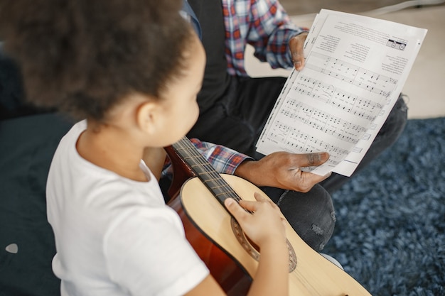 Foto gratuita padre con hija en el sofá. chica sosteniendo una guitarra. aprendiendo a tocar la guitarra.