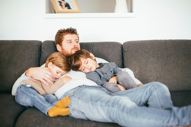 Padre con hijos siestas en sofá