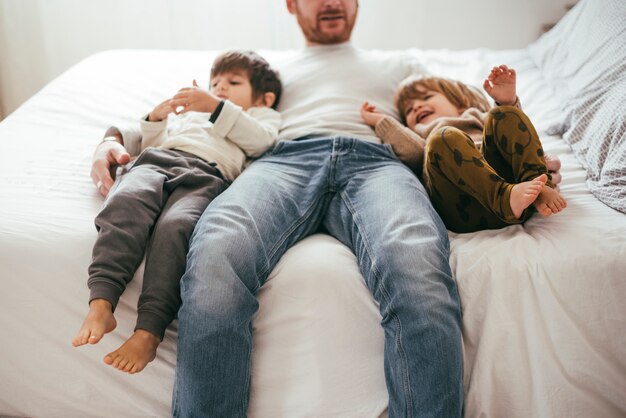 Padre juguetón en la cama con hijos.