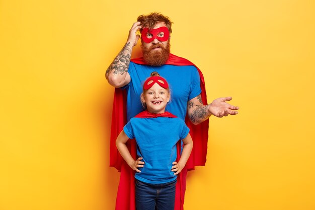Padre juguetón con hija pequeña usan disfraces de superhéroe, juegan juntos en casa