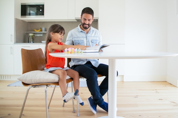 Padre latino sosteniendo un libro para su hija y sonriendo.