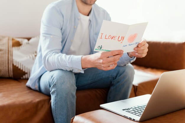 Padre leyendo la tarjeta del día del padre mientras trabaja en la computadora portátil