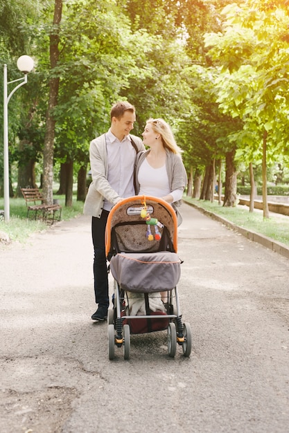 Foto gratuita padre y madre joven paseando a su bebé por el parque en un carrito