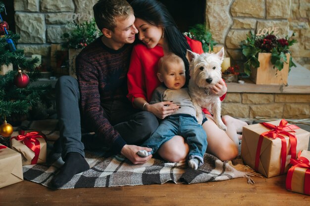 Padre y madre con su bebé y el perro sentados en el suelo