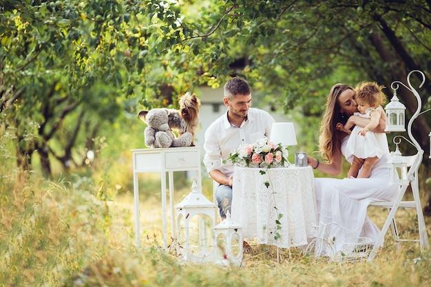 Padre y madre con su hija en mitad del campo con mesa y sillas blancas