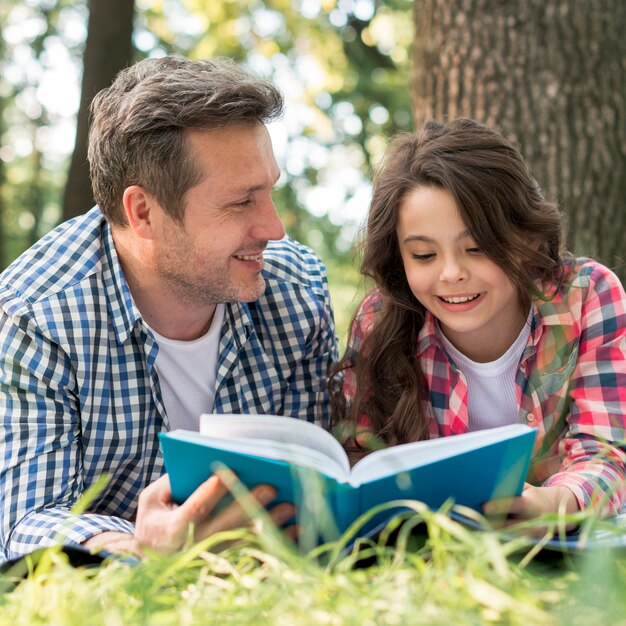 Padre mirando a su hija mientras lee un libro en el parque