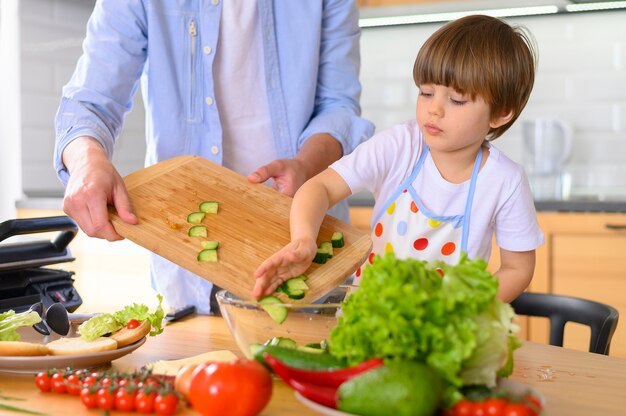 Padre monoparental y niño poniendo verduras en un tazón