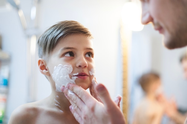 Padre poniendo espuma de afeitar en la cara de su hijo