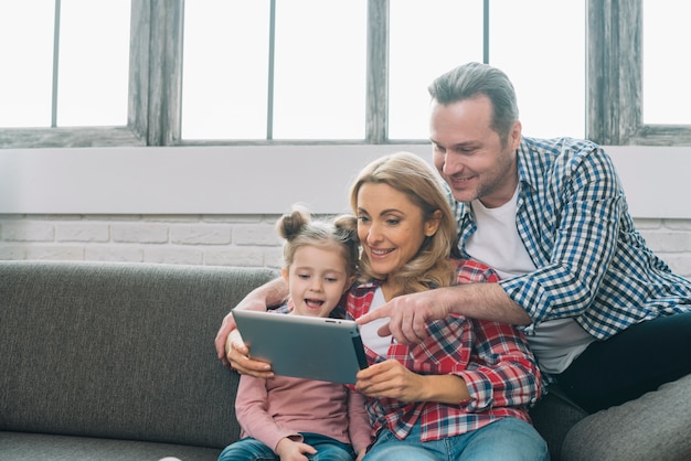 Padre que señala en la tableta digital con su esposa e hija sonrientes en casa