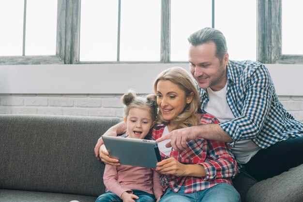 Padre que señala en la tableta digital con su esposa e hija sonrientes en casa