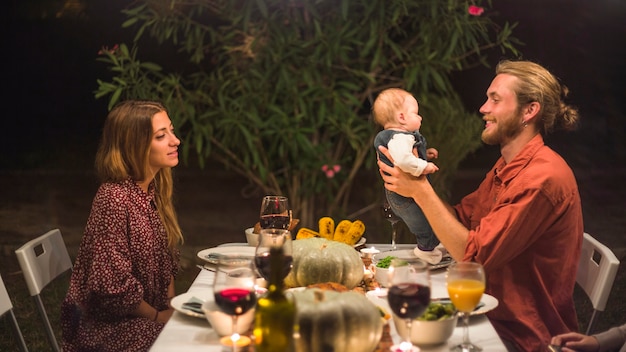 Padre sosteniendo pequeño bebé cerca de dama en la cena familiar